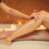 Side-view of a beautician’s hands gently smoothing a woman’s legs as she lies on a treatment bed in a salon after a wax