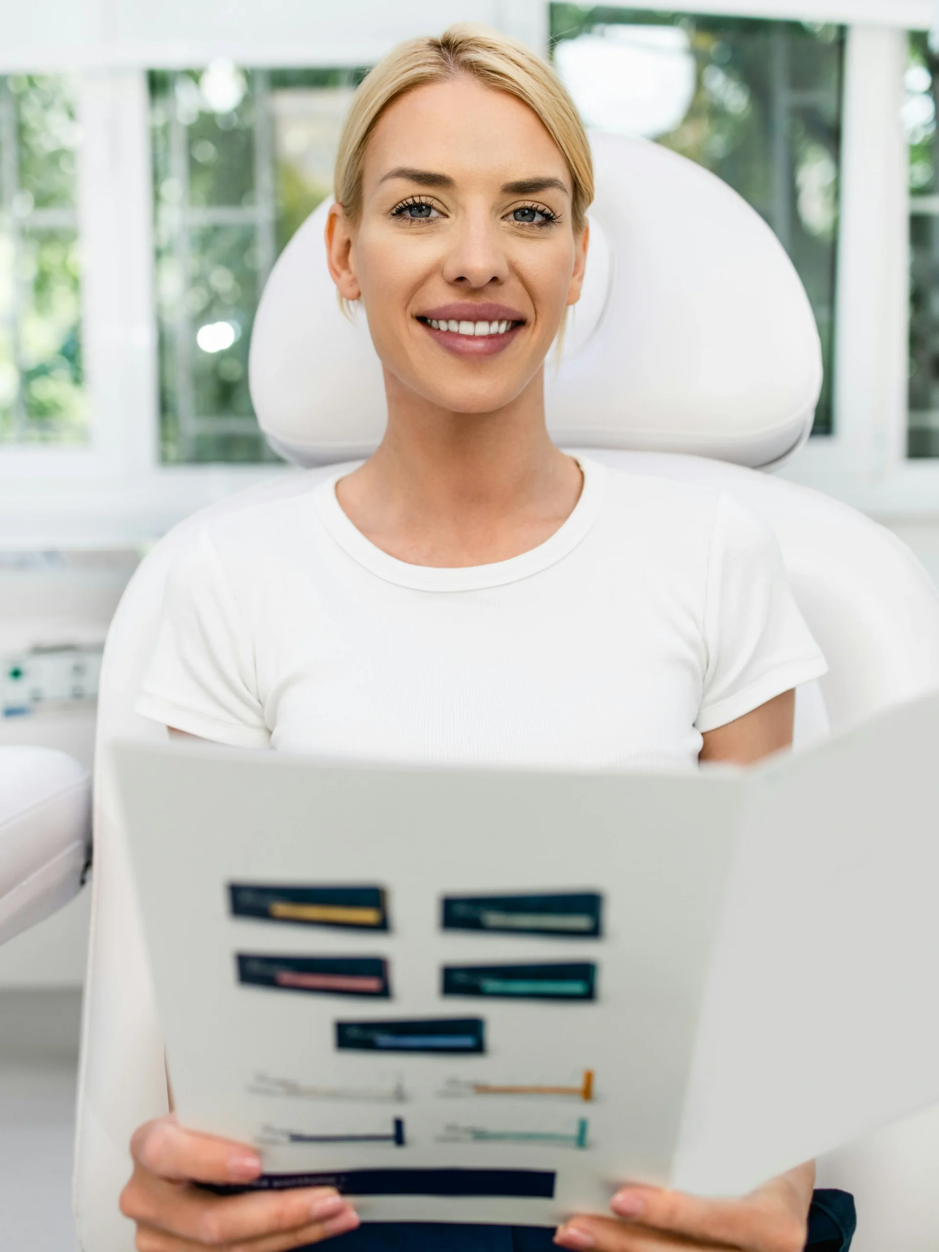 A client sits in a bright, clean clinic smiling as she holds an information booklet about facial treatments