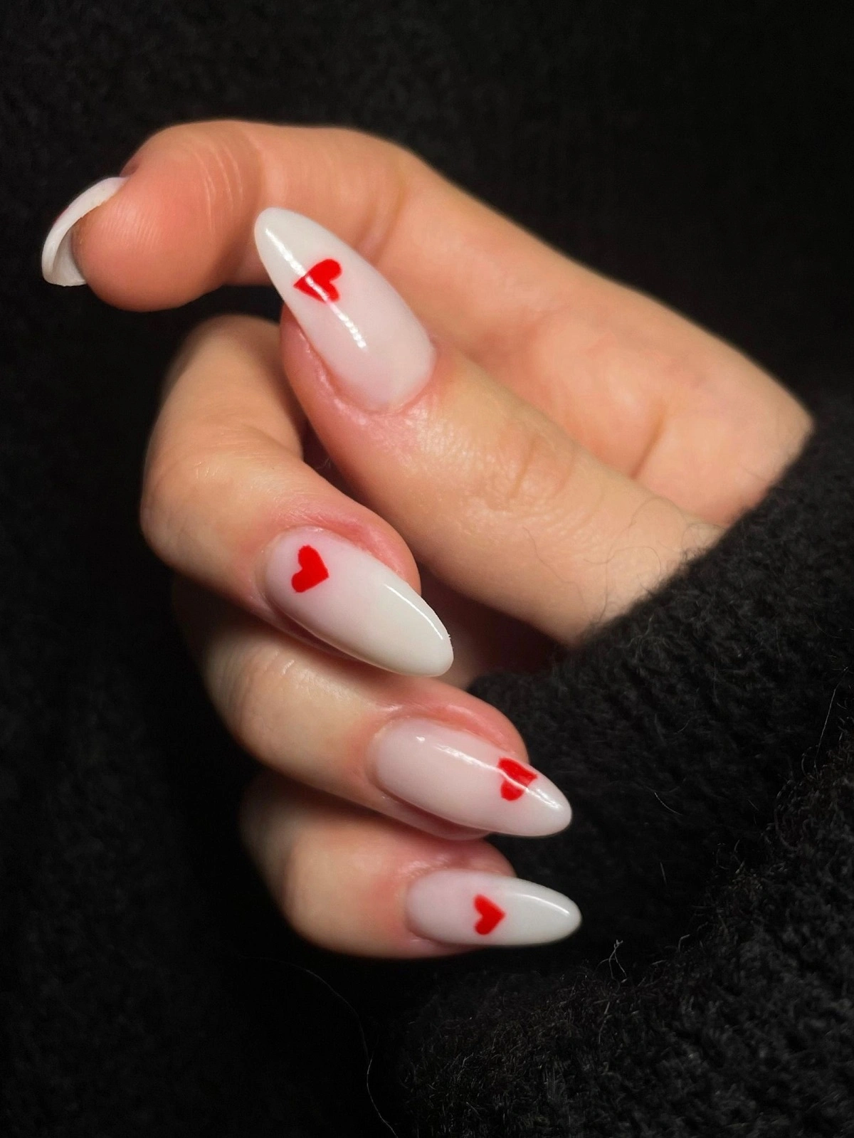 Close-up of a woman’s hand with white almond-shaped acrylic nails decorated with small red hearts