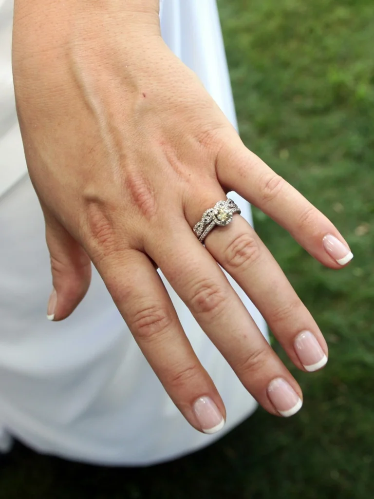 A woman’s hand showing a neat French tips manicure with a classic nude and white combination on short squoval nails